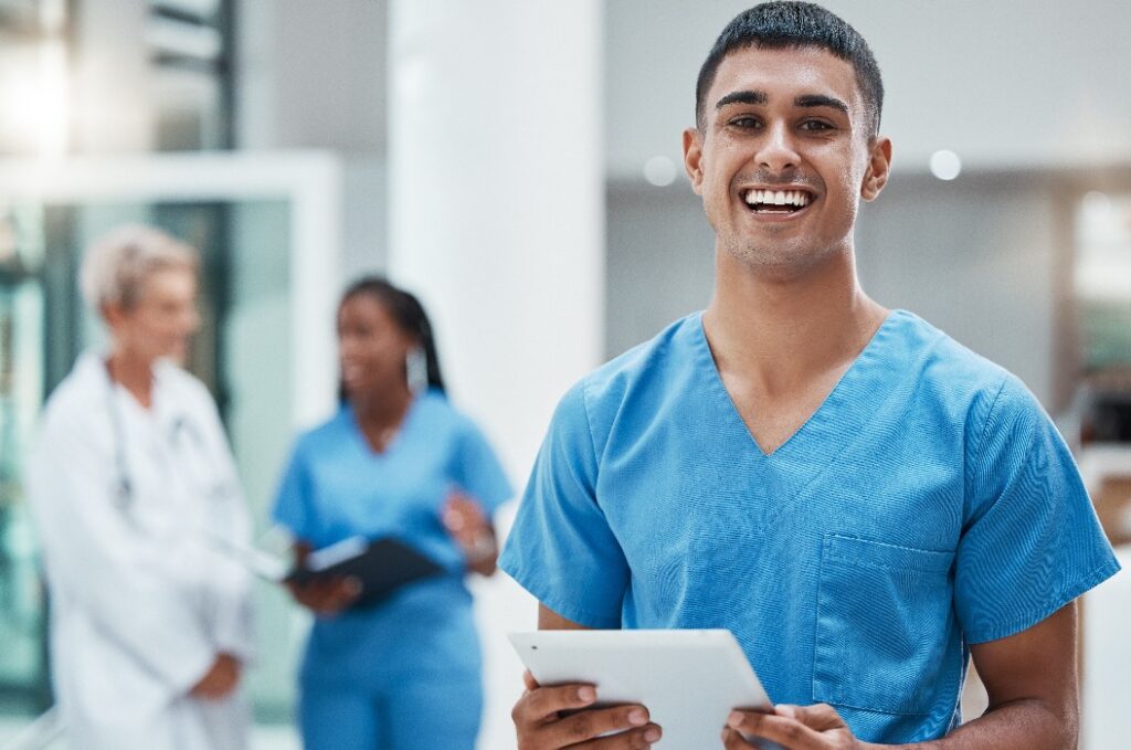 Tablet, Gesundheitswesen und Medizin: Ein Pfleger recherchiert in einem Krankenhaus zu Gesundheitsfragen oder Behandlungsmethoden. Medizin, Versicherungen und Krankenversicherung: Ein junger männlicher Klinikmitarbeiter führt eine Online-Recherche durch